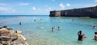A shallow water area on a beach with a crowd of people swimming.
